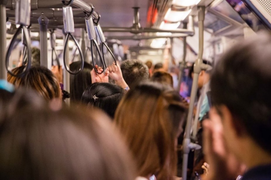 Image of the interior of a full train with many people standing and holding on to supports.